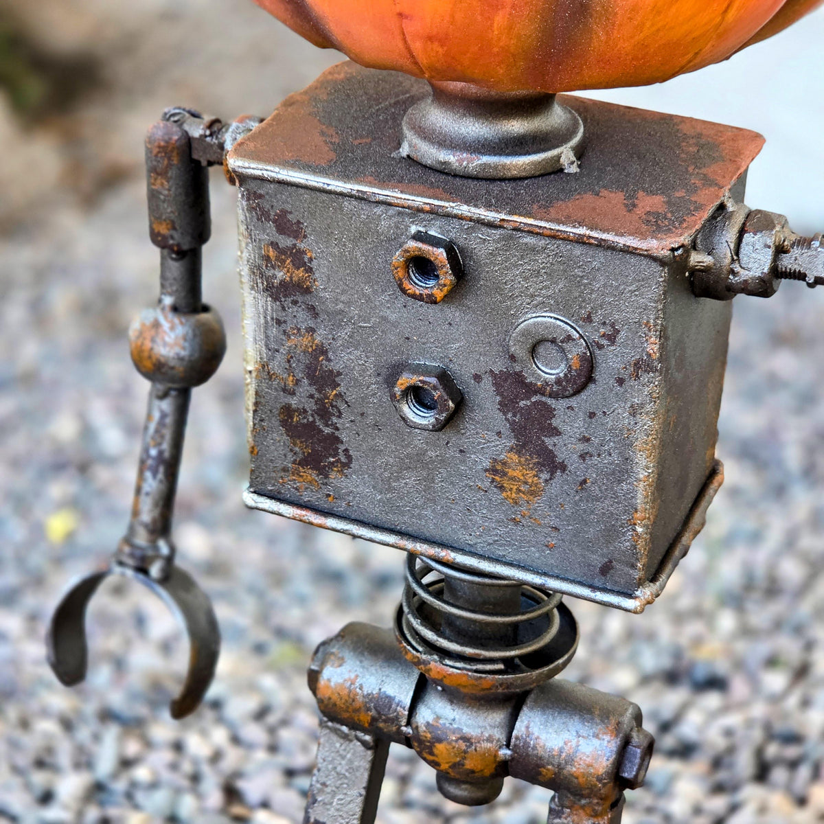 A close-up view of a rusted metal robot sculpture with a pumpkin-shaped headpiece.