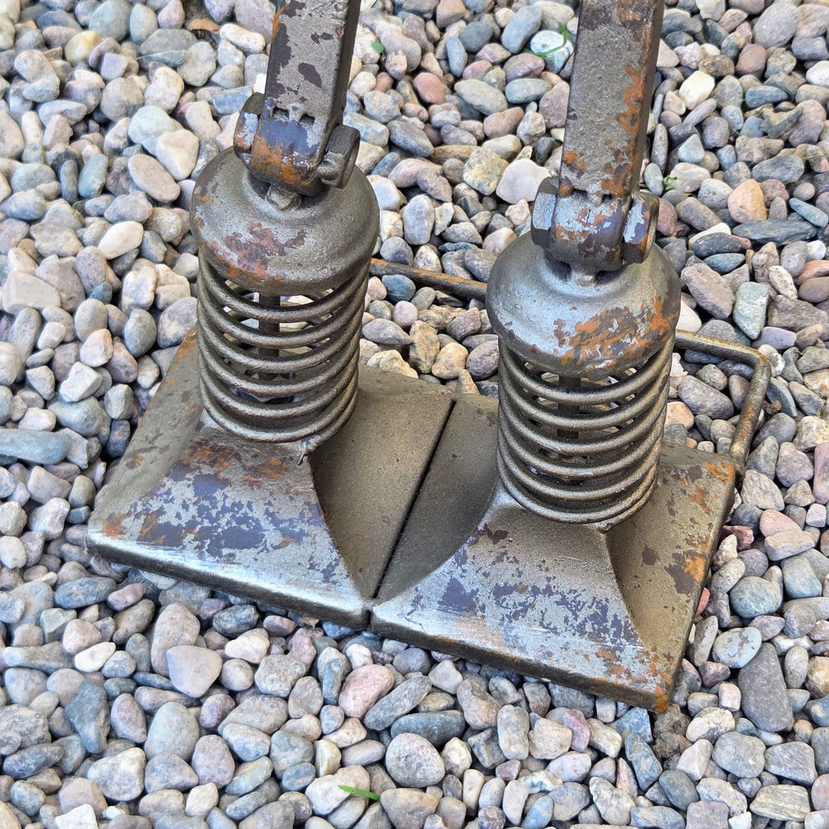 a pair of rusted metal poles or supports, one on top of the other, standing on a bed of small rocks or pebbles.