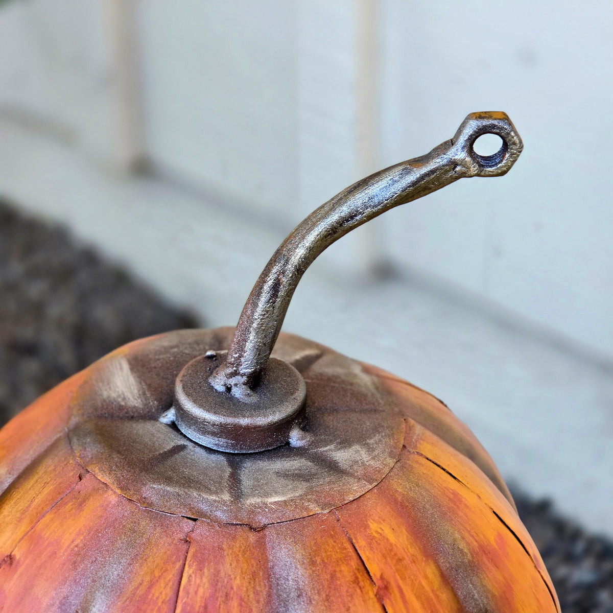 a close-up view of a metal object resembling a pumpkin or a similar orange-colored vegetable, with a curved metal piece attached to it.