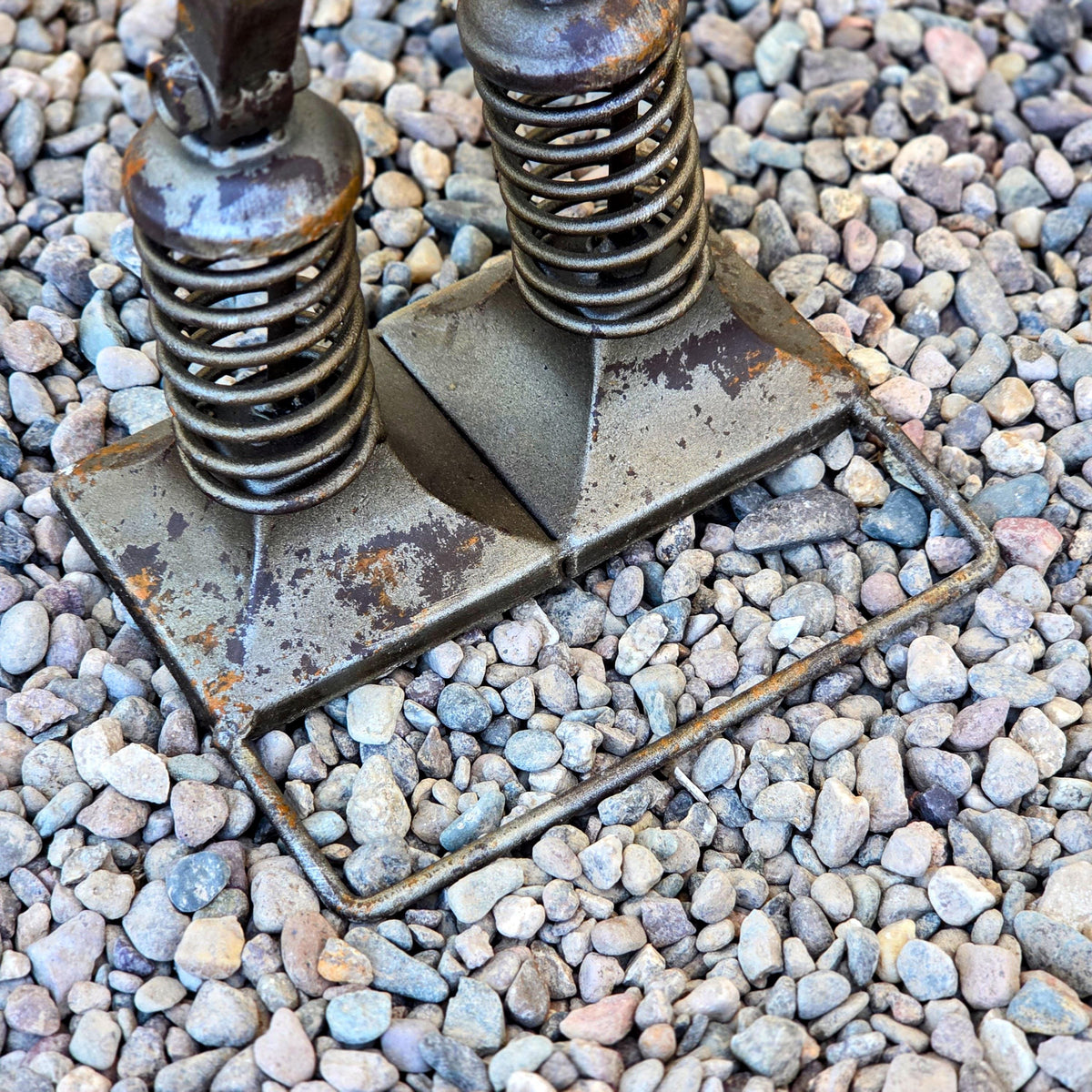 a close-up view of a metal spring-loaded device resting on a bed of small pebbles or gravel.